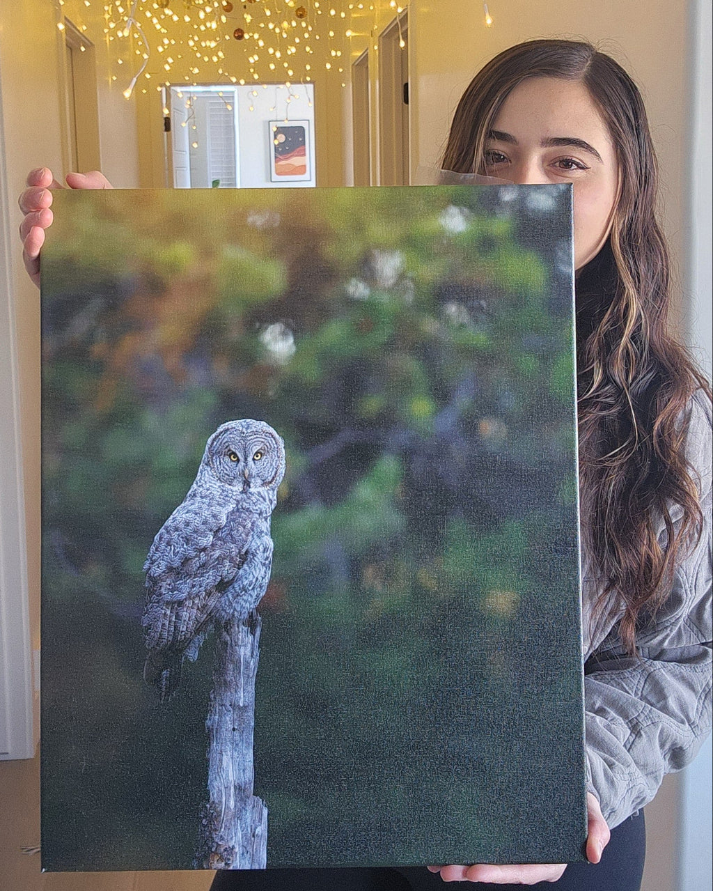 Person holding a canvas of a great gray owl in front of a hallway with lights.