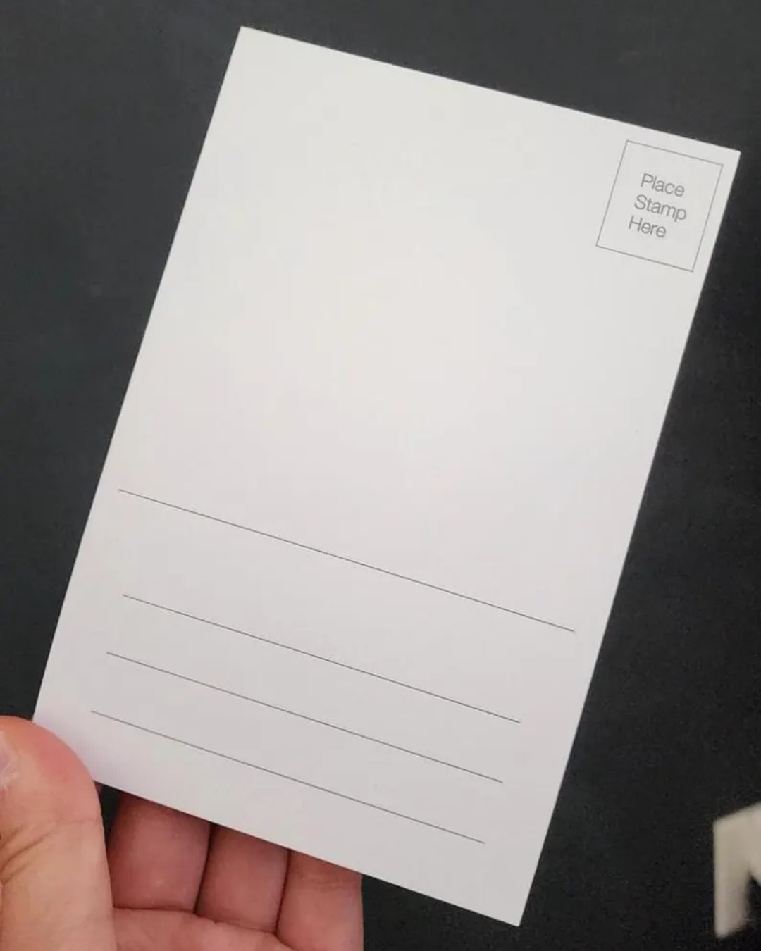 White postcard with lined writing area held by a hand against a black background